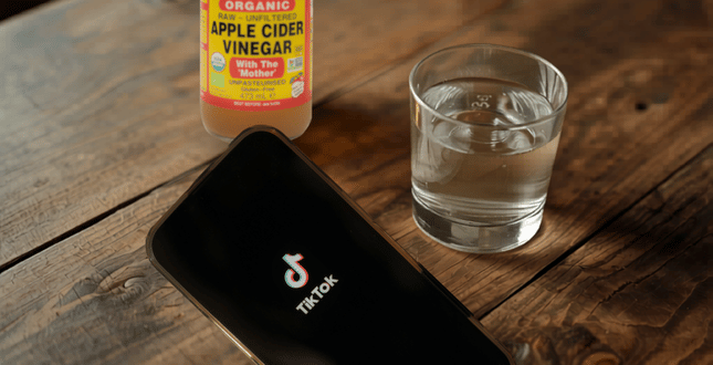 Smartphone met TikTok naast een fles biologische appelazijn en een glas water op een houten tafel
